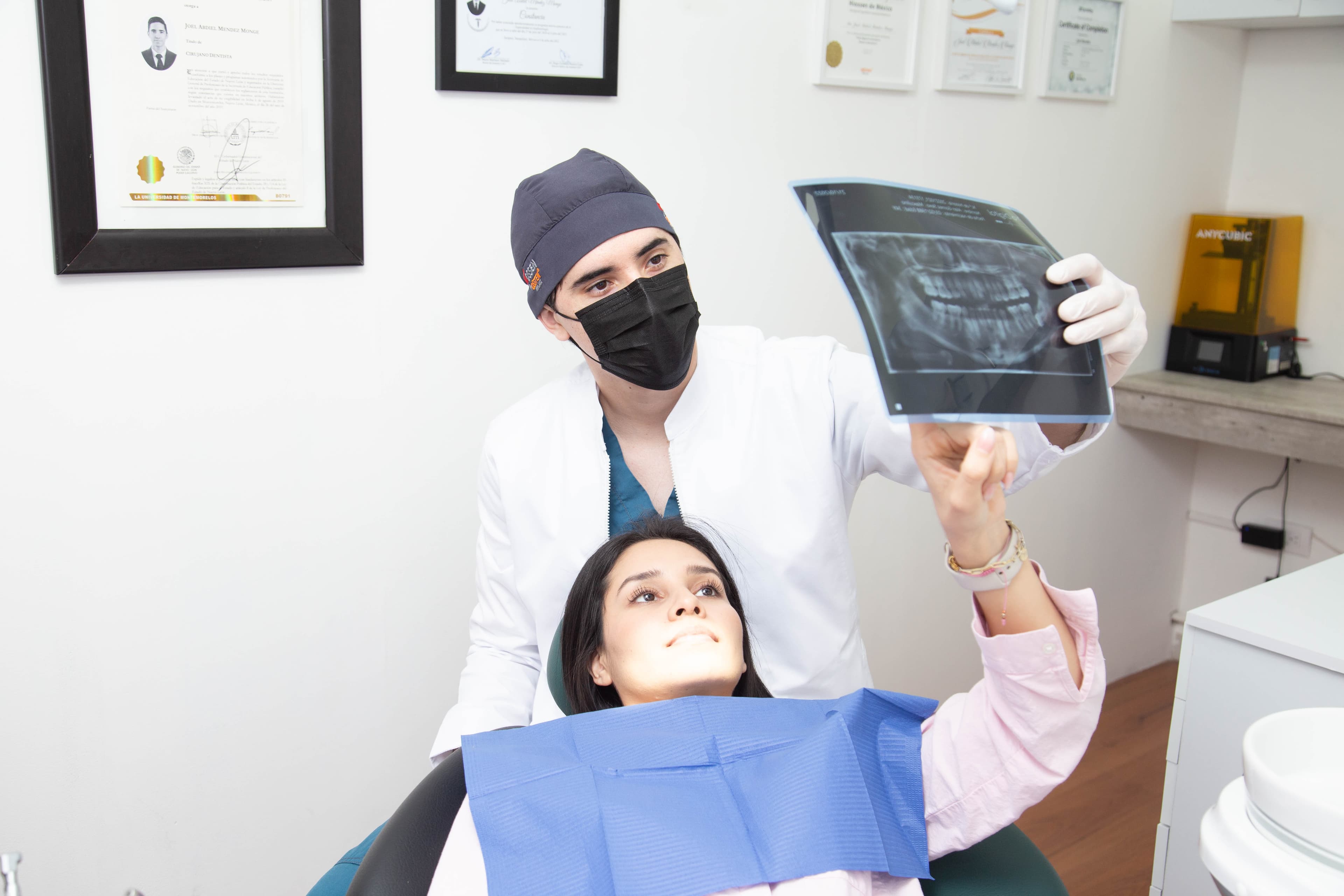 Dr. Joel presentando una radiografía con diplomas profesionales de fondo